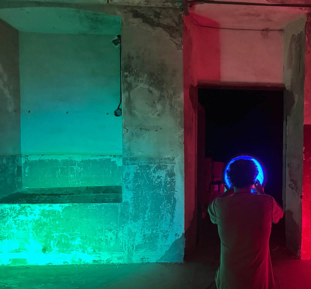 A figure silhouetted in a doorway of the factory, walls washed in green and red light